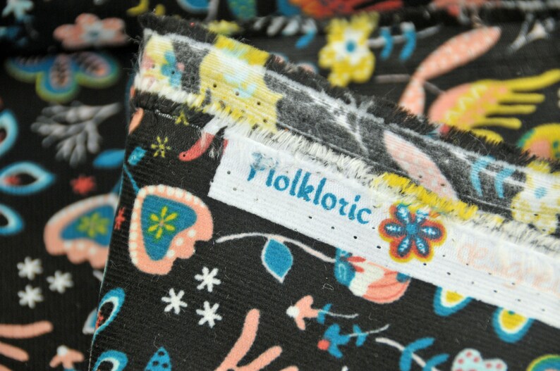 May include: Close-up of black fabric with a colorful floral pattern. The fabric has a white label with the word "Folkloric" printed on it.