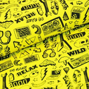 Könnte beinhalten: Gelber Stoff mit einem schwarz-weißen Druck verschiedener Kritzeleien, darunter ein Schädel, Blitze, eine Gitarre, Kopfhörer und die Wörter "Dude", "Relax", "Let's Go" und "Wild".