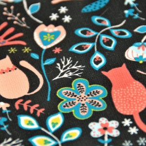 May include: Black fabric with a repeating pattern of pink and blue stylized flowers, leaves, and cats. The cats are wearing collars with red and white accents.