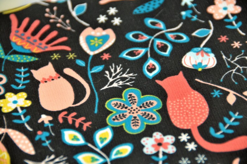 May include: Black fabric with a repeating pattern of pink and blue stylized flowers, leaves, and cats. The cats are wearing collars with red and white accents.