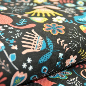 May include: Black fabric with a repeating pattern of stylized flowers, cats, and leaves in shades of pink, blue, yellow, and white.