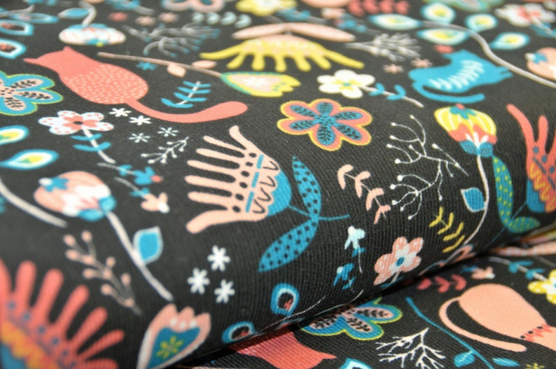 May include: Black fabric with a repeating pattern of stylized flowers, cats, and leaves in shades of pink, blue, yellow, and white.