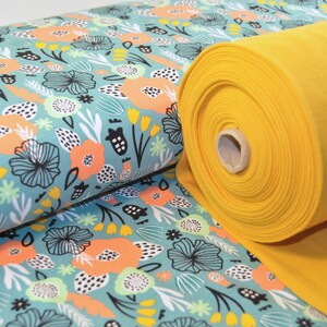 Puede incluir: Un rollo de tela amarilla con una tela de estampado floral azul verdoso y blanco debajo. El estampado floral presenta flores abstractas, hojas y puntos.