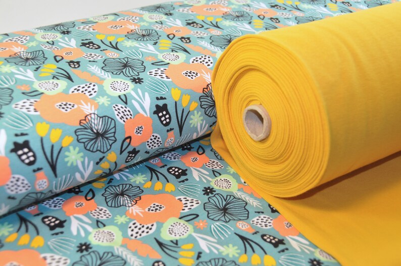 Puede incluir: Un rollo de tela amarilla con una tela de estampado floral azul verdoso y blanco debajo. El estampado floral presenta flores abstractas, hojas y puntos.