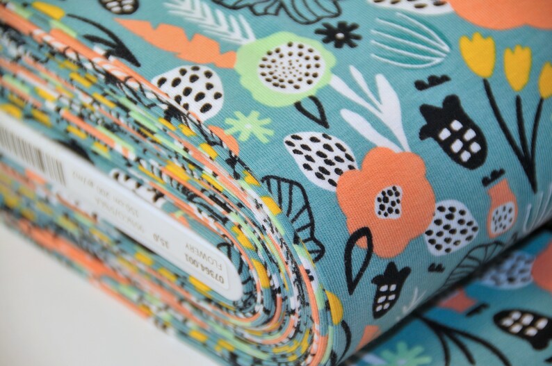 Puede incluir: Un rollo de tela turquesa con un estampado floral colorido que incluye naranja, amarillo, blanco y negro. La tela tiene un patr&oacute;n repetitivo de flores, hojas y formas geom&eacute;tricas.