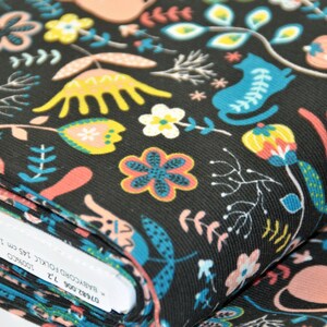 May include: Black fabric with a colorful floral and cat print. The fabric is folded and the label reads "BABYCORDUROY FOLKIC 100%COTTON 145 cm 1.55 m/1.72"