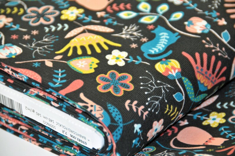 May include: Black fabric with a colorful floral and cat print. The fabric is folded and the label reads "BABYCORDUROY FOLKIC 100%COTTON 145 cm 1.55 m/1.72"