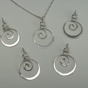 May include: A set of four silver pendant necklaces with a hammered circular design and a spiral detail. The pendants are of varying sizes.