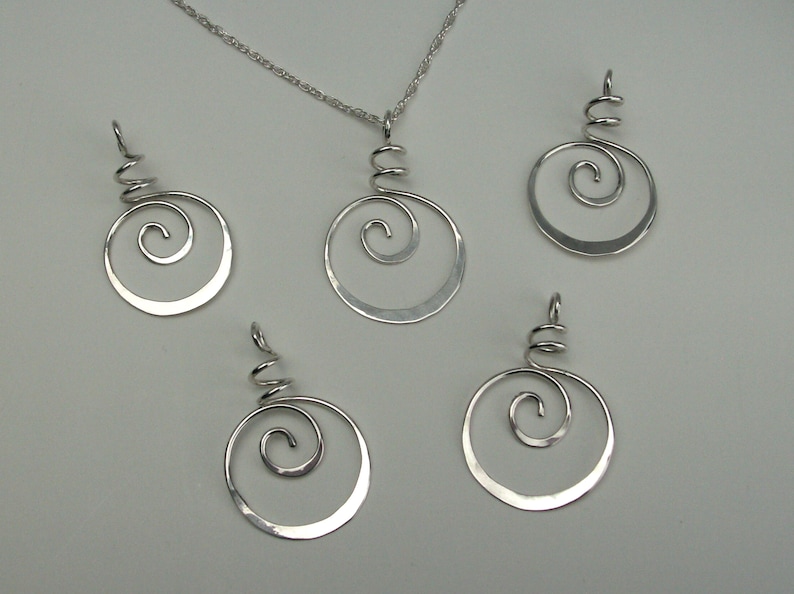 May include: A set of four silver pendant necklaces with a hammered circular design and a spiral detail. The pendants are of varying sizes.