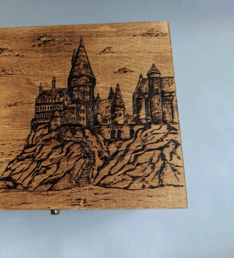 May include: A wooden box with a burnt-in image of Hogwarts castle, a fictional school of witchcraft and wizardry from the Harry Potter series.