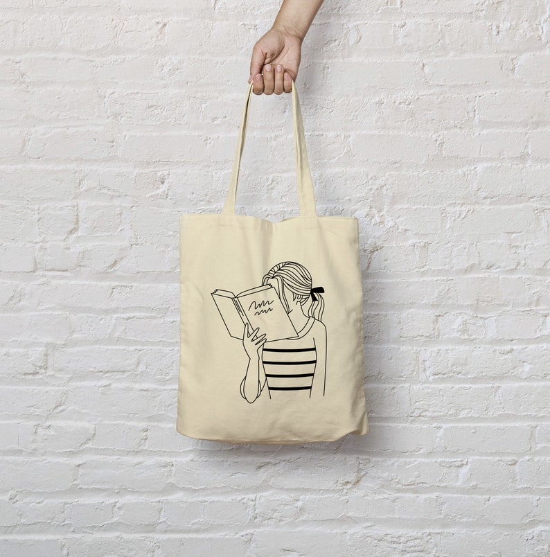 May include: A beige tote bag with a black line drawing of a person reading a book. The book has the word "Time" written on the cover.