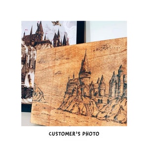 May include: A wood burned image of Hogwarts castle on a wooden plaque. The image is in black and white and shows the castle on a cliff overlooking a body of water.