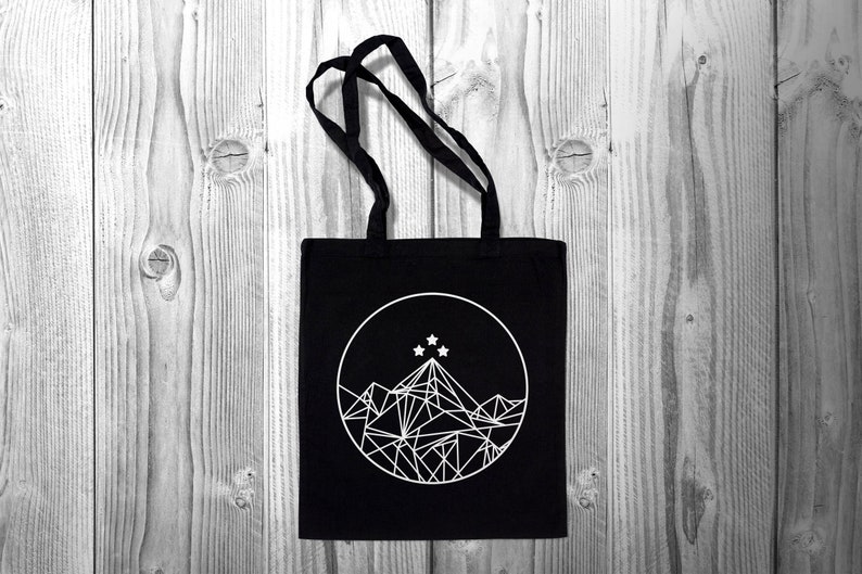 May include: Black canvas tote bag with a white geometric mountain design and five white stars in a circle.
