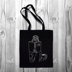 May include: Black tote bag with a white outline of a person reading a book and holding a cup of coffee. The book has the text "Read more" on the cover.