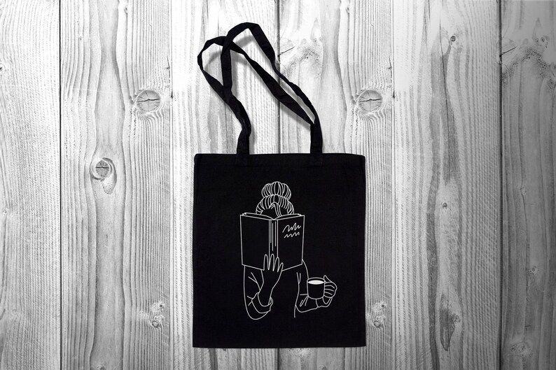 May include: Black tote bag with a white outline of a person reading a book and holding a cup of coffee. The book has the text "Read more" on the cover.