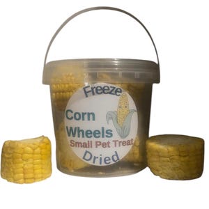 May include: A clear plastic container filled with dried corn wheels for small pets. The container has a handle and a label that reads "Freeze Corn Wheels Small Pet Treat Dried." Two corn wheel pieces are next to the container.
