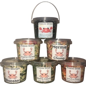 May include: Six containers of freeze-dried food for hermit crabs. The containers are labeled with different flavors, including "Tropical Garden", "Hermie Chomp", "Shell Strength Booster", "Molting Support", and "Immune & Vitality".