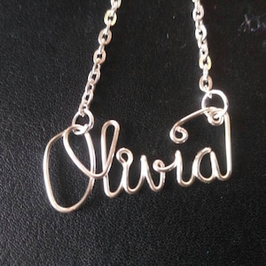 Puede incluir: Collar de plata con el nombre Olivia escrito en alambre.