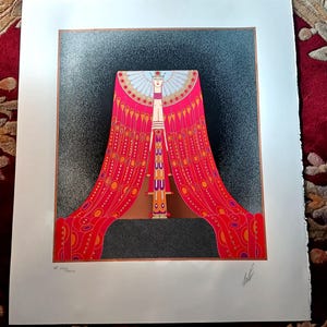 May include: Art Deco style print featuring a stylized figure with a red and gold draped garment. The artwork has a black and gray speckled background and a brown border. The figure has a white face and a decorative headdress.