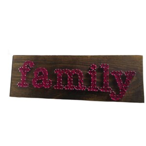 Op de afbeelding: Een houten bord met het woord "familie" gespeld in roze touwkunst.