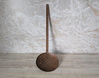 May include: A rustic, antique metal skimmer with a long handle and a round, perforated bowl. The skimmer is made of a dark, aged metal, showing signs of wear. The handle has a decorative twisted design.