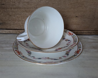 May include: A white teacup and two matching saucers with a floral design and gold trim. The teacup is resting on the saucers. The teacups and saucers are vintage and appear to be made of porcelain.