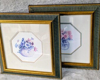 May include: Two framed floral art prints. Each print features a watercolor painting of flowers in a vase. The frames are dark green with gold inner edges. The artwork is set against a white background.