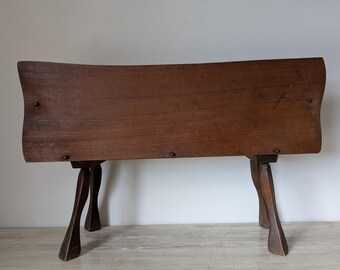 May include: A dark brown wooden bench with a curved back and four angled legs. The bench is made of solid wood and has a natural finish. The legs are carved and add a unique design element. The bench is approximately 48 inches long.