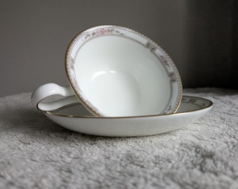 May include: White teacup and saucer set with gold trim and a decorative border featuring floral and geometric patterns. The teacup is resting on the saucer, showcasing the elegant design.