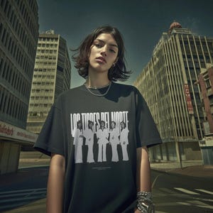 May include: A black t-shirt with the text "LOS TIGRES DEL NORTE" in white block letters. Below the text is a black and white image of five people in white suits. The person in the image is wearing silver jewelry.