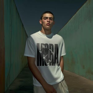 May include: A white crew neck t-shirt featuring a black and white graphic of a person in motion, with the word "MORA" printed in large black letters. The shirt is paired with light-colored pants.