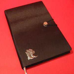 Peut inclure: Un journal en cuir noir avec un motif de botte de cowboy et de chapeau argenté sur le devant. Le journal a une fermeture à bouton argenté et un élastique noir.