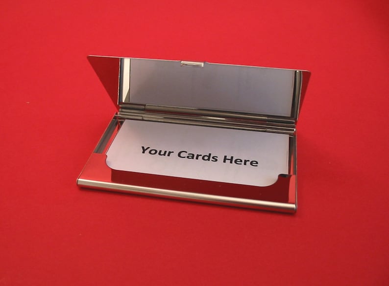 Puede incluir: Un porta tarjetas de metal plateado con una tarjeta blanca en el interior que dice "Your Cards Here".