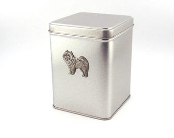 Op de afbeelding: Een zilveren metalen blik met een klein tinnen beeldje van een Chow Chow op de voorkant.