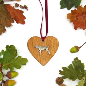 May include: A wooden heart-shaped ornament featuring a silver dog silhouette. The ornament is suspended from a red ribbon and surrounded by autumn leaves and acorns.