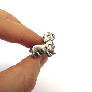Puede incluir: Una figurita de dachshund de plata, una raza de perro popular, se muestra de perfil. La figurita es detallada y realista, con un acabado liso y met&aacute;lico.