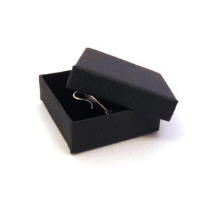 May include: A black gift box with a black lid, the lid is open and a silver ring is inside the box.