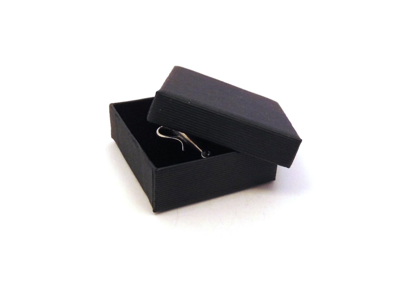 May include: A black gift box with a black lid, the lid is open and a silver ring is inside the box.