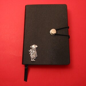 Peut inclure: Journal en cuir noir avec un charme de souris argenté et une fermeture élastique noire avec un bouton argenté.