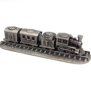 May include: A silver pewter train engine and three train cars on a track. The train cars have holes on the top and are likely salt and pepper shakers.