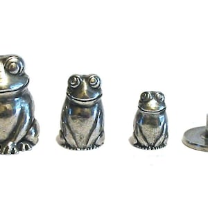 May include: Set of four silver-toned frog-shaped thimbles. The thimbles are different sizes, with the largest thimble being about 5 cm tall. The smallest thimble is about 2.5 cm tall. The thimbles are all sitting on a white surface.