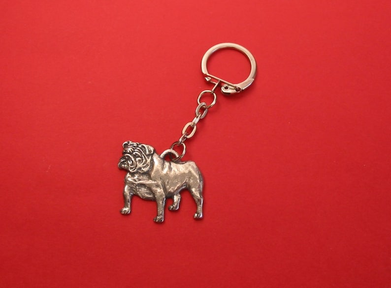 May include: Silver bulldog keychain with a silver chain and a silver ring. The bulldog is standing on all four legs and has a detailed face.