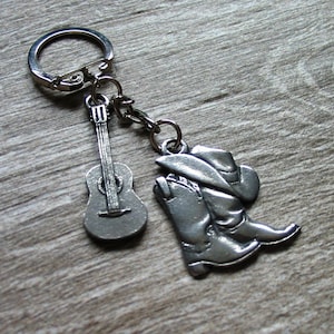 Könnte beinhalten: Silberner Schlüsselanhänger mit einem Gitarren- und einem Cowboy-Stiefel-Anhänger. Der Stiefel trägt einen Cowboyhut.