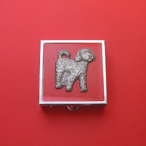 May include: A silver dog figurine on a red square, set within a silver frame. The dog has a textured appearance. The background is a solid red colour. The item appears to be a decorative box or trinket holder.