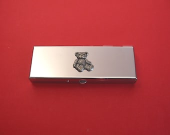 May include: A silver metal pill box with a small pewter teddy bear design on the lid.