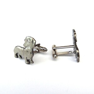 Puede incluir: Un par de gemelos de plata con la silueta de un dachshund. Los gemelos est&aacute;n hechos de metal y tienen un acabado pulido.