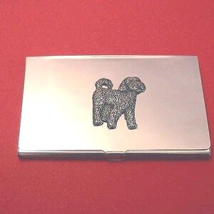May include: A rectangular silver-toned metal business card holder featuring a centred, detailed black engraved illustration of a curly-coated dog standing in profile. The surface of the case is smooth and reflective with a polished metallic finish.