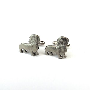 Puede incluir: Un par de gemelos de plata con forma de dachshund. Los gemelos est&aacute;n hechos de metal y presentan un dise&ntilde;o de dachshund detallado.