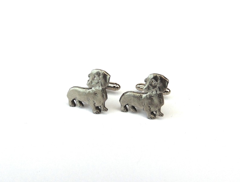 Puede incluir: Un par de gemelos de plata con forma de dachshund. Los gemelos est&aacute;n hechos de metal y presentan un dise&ntilde;o de dachshund detallado.