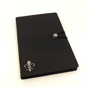 May include: A black leather journal with a silver fleur-de-lis design and a silver button closure.
